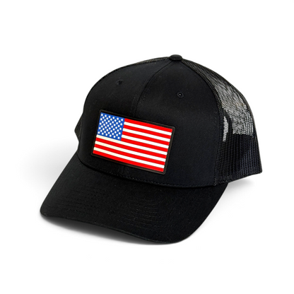 Crafted Merch black trucker hat featuring a rectangular American flag PVC patch and breathable mesh back panel.