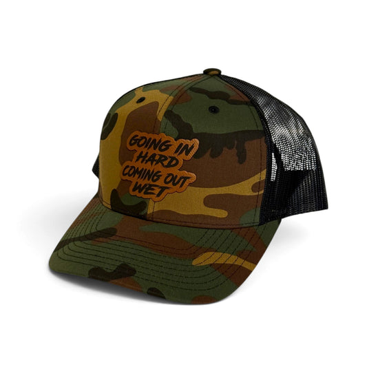 Crafted Merch trucker hat in camo print with a brown patch featuring the text Going In Hard Coming Out Wet