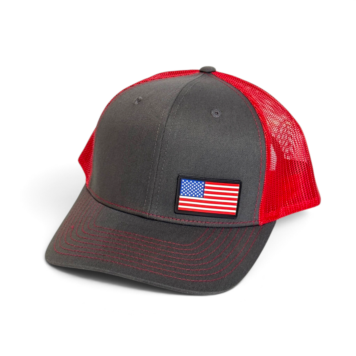 Crafted Merch American flag PVC patch trucker hat in charcoal grey with a vibrant red mesh back and red stitching.