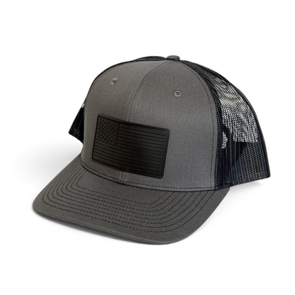 Crafted Merch grey trucker hat with a black monochromatic American flag PVC patch and breathable mesh back