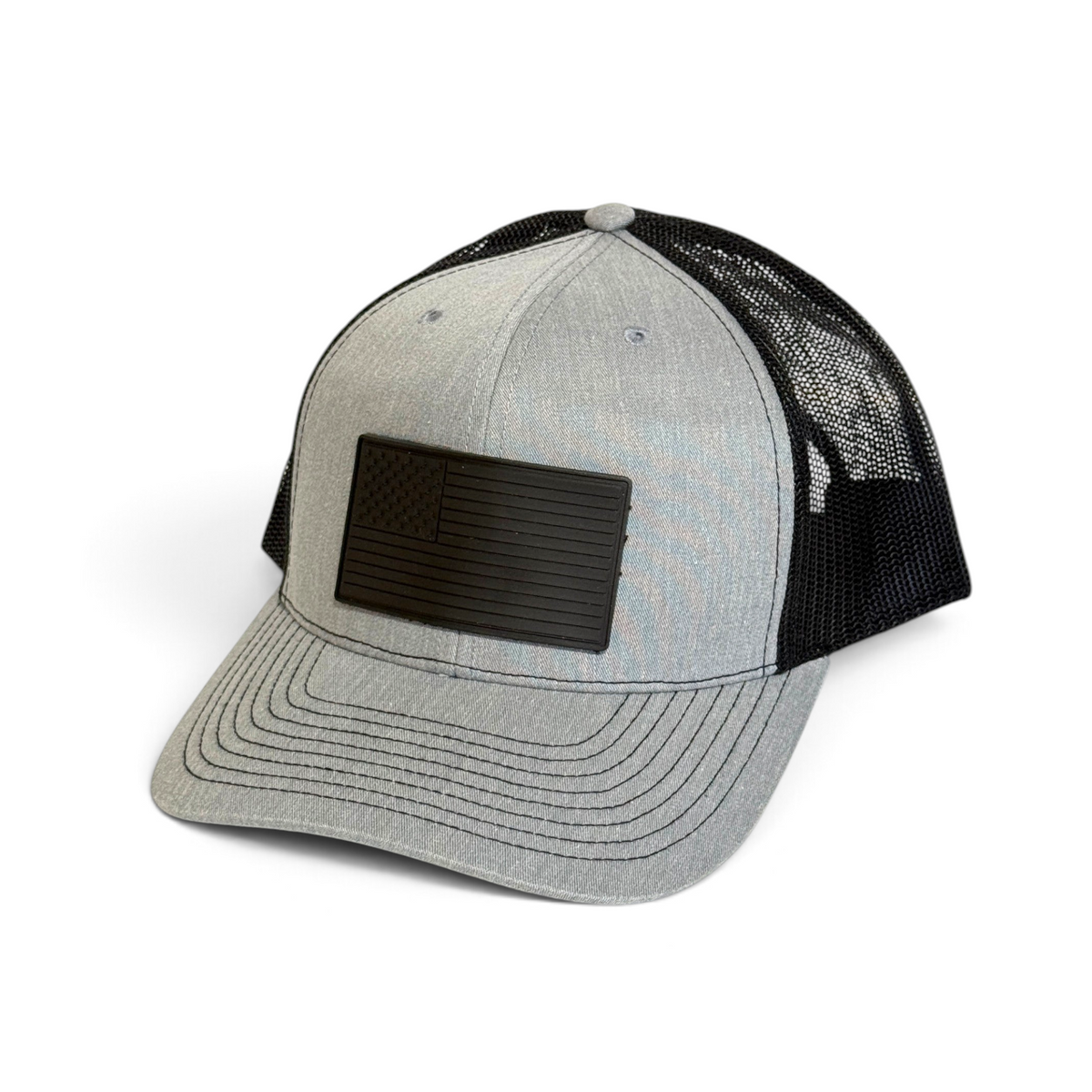 Crafted Merch grey and black trucker hat featuring a monochromatic American flag PVC patch and breathable mesh back.