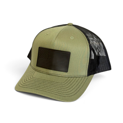 Crafted Merch olive green and black trucker hat featuring a monochromatic American flag PVC patch and mesh back