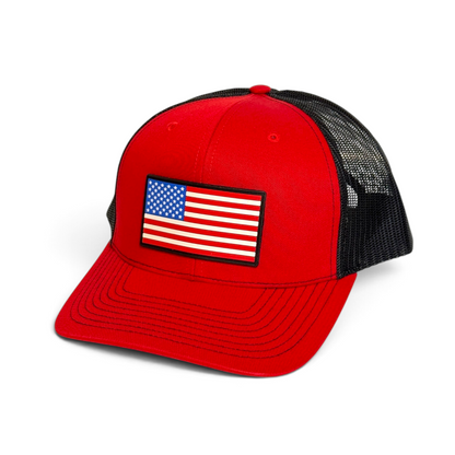 Crafted Merch red trucker hat with a black mesh back and a rectangular American flag PVC patch on the front panel.
